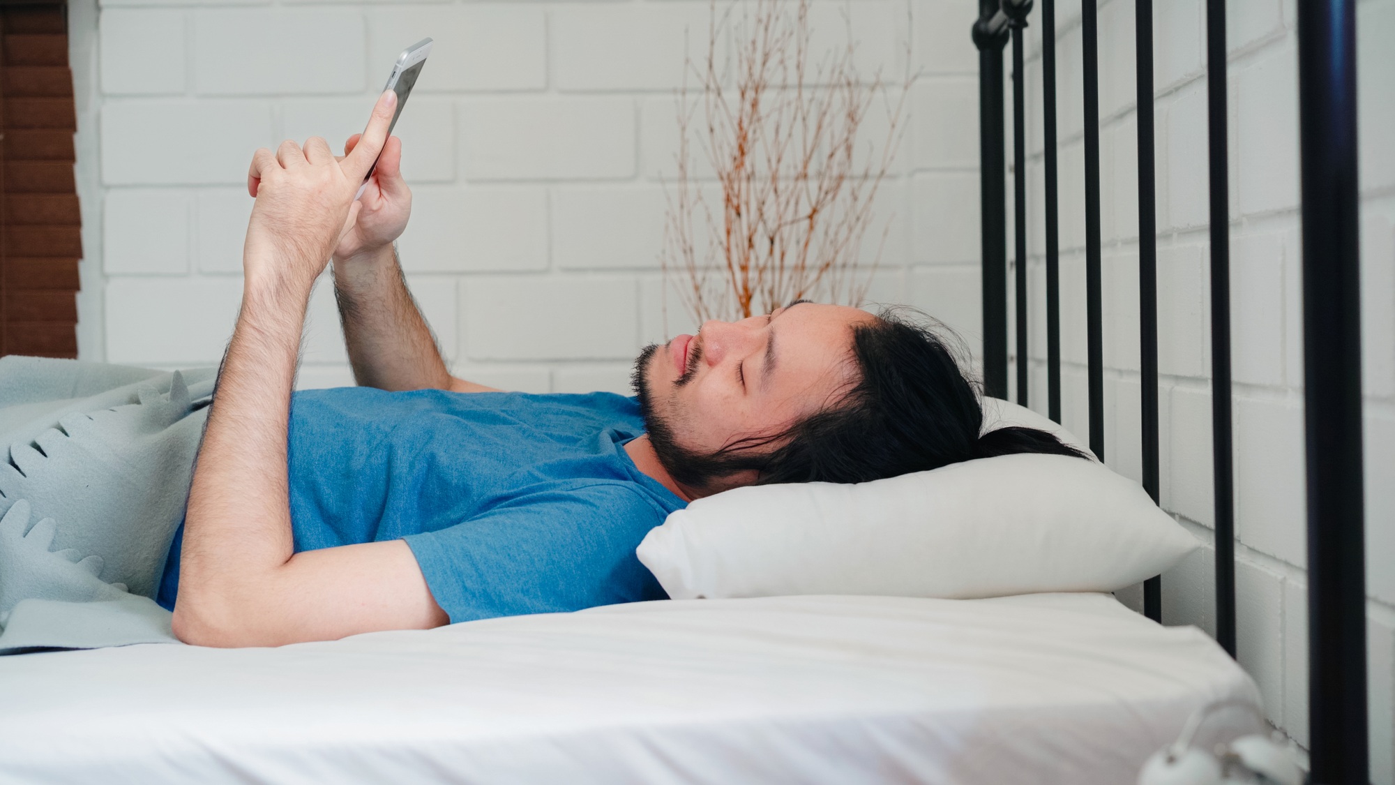 Asia male using mobile phone check social media and send message after awake on bed.