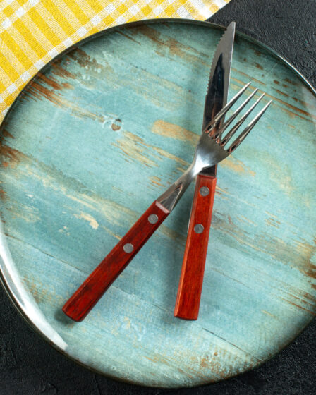 Horizontal view of meal cutlery in cross on a blue plate and yellow stripped towel on dark