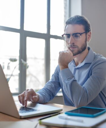 Young smart man with glasses looking at a laptop.