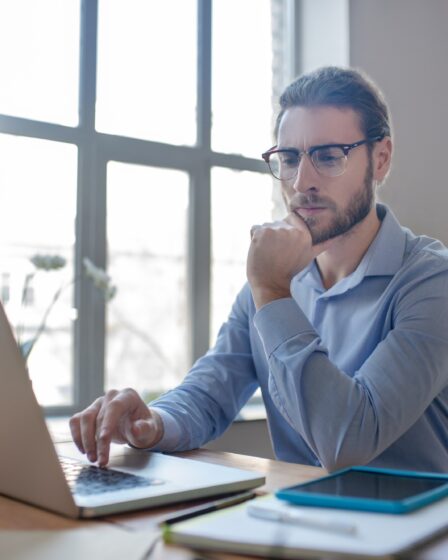 Young smart man with glasses looking at a laptop.